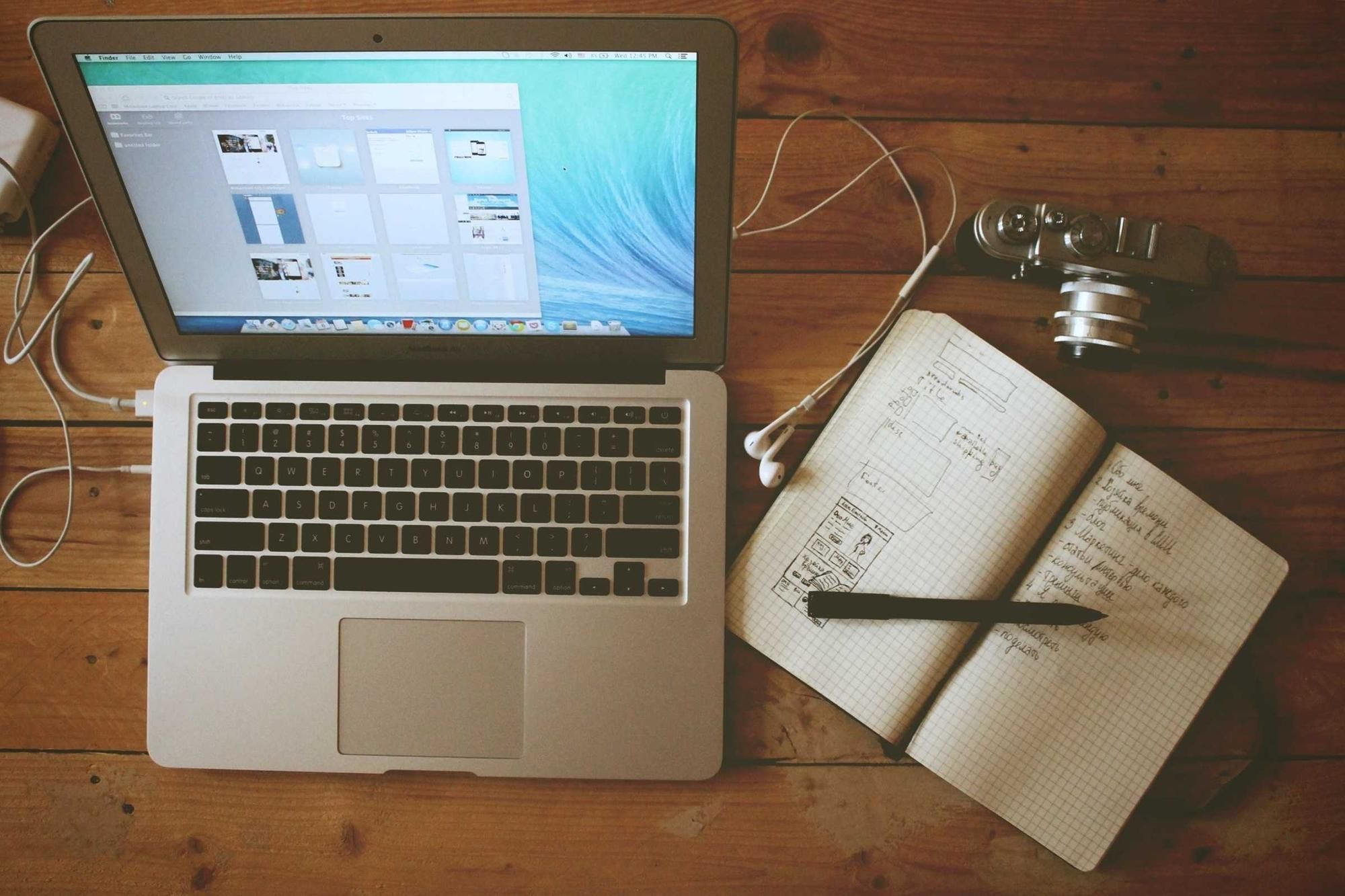 Laptop, notebook and camera on a wooden desk seen from above